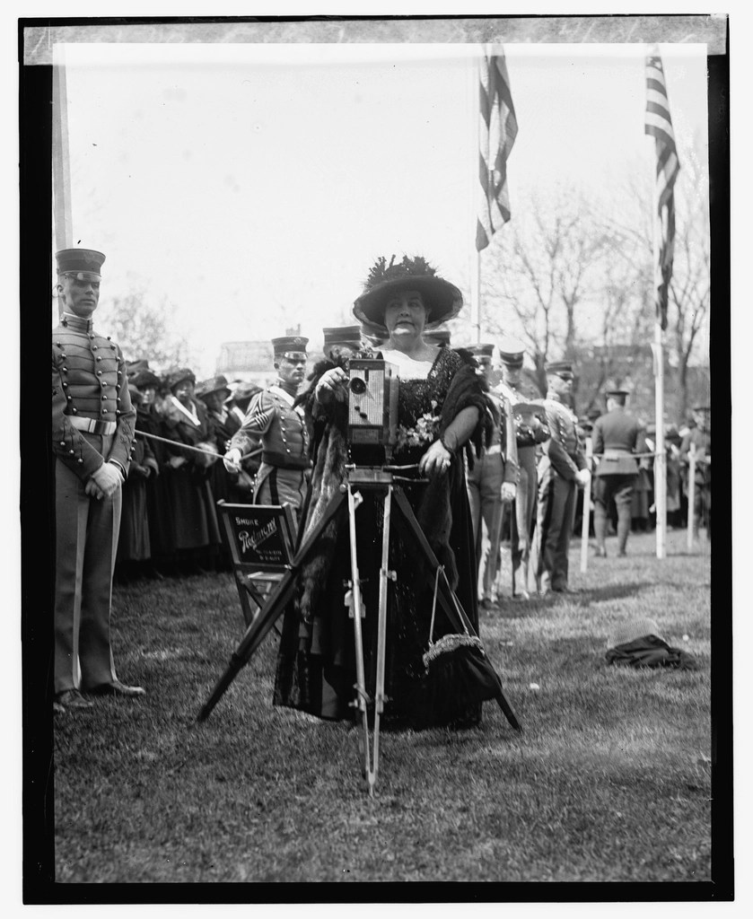 1900'lerin başında üniformalı askerler arasında kamera ile fotoğraf çeken şapkalı kadın