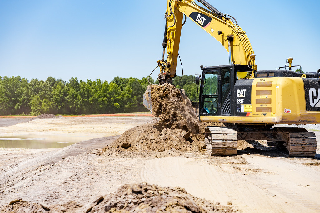 Açık şantiyede çalışan sarı Caterpillar ekskavatör kum yığını kazıyor