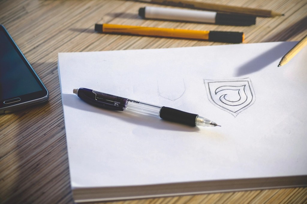 Ahşap Çalışma Masasında Kalemle Çizilmiş Logo Tasarım Eskizi ve Araçlar