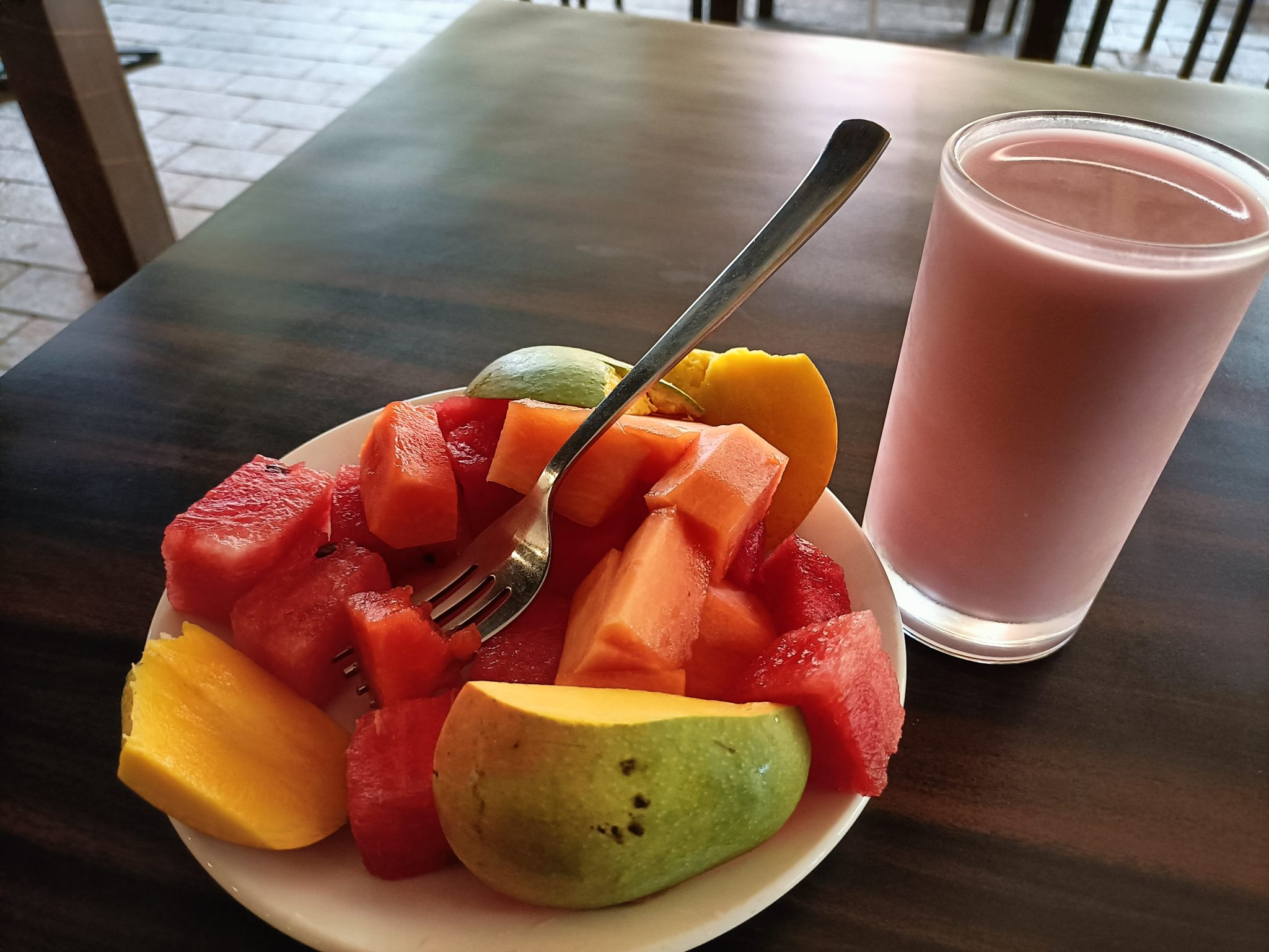 ahşap masada karpuz papaya mango dilimleri ve pembe smoothie ile kahvaltı
