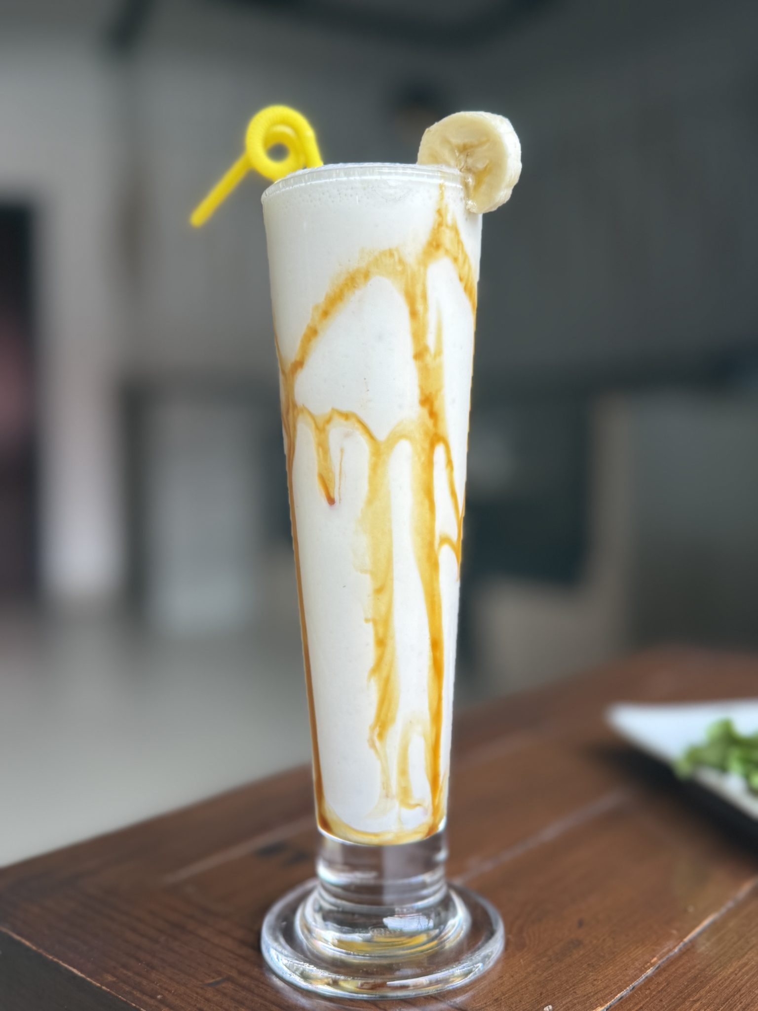 Ahşap masada uzun bardakta karamel soslu muzlu milkshake sunumu