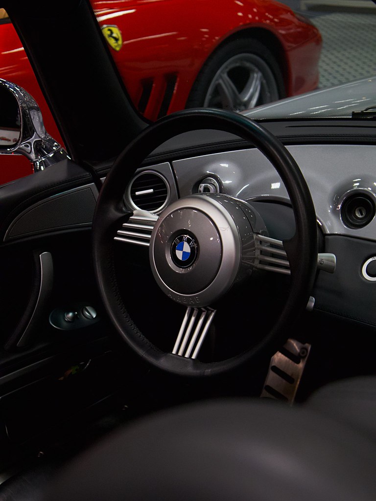 bmw direksiyonu ve arka plandaki kırmızı ferrari ile lüks spor araba koleksiyonu