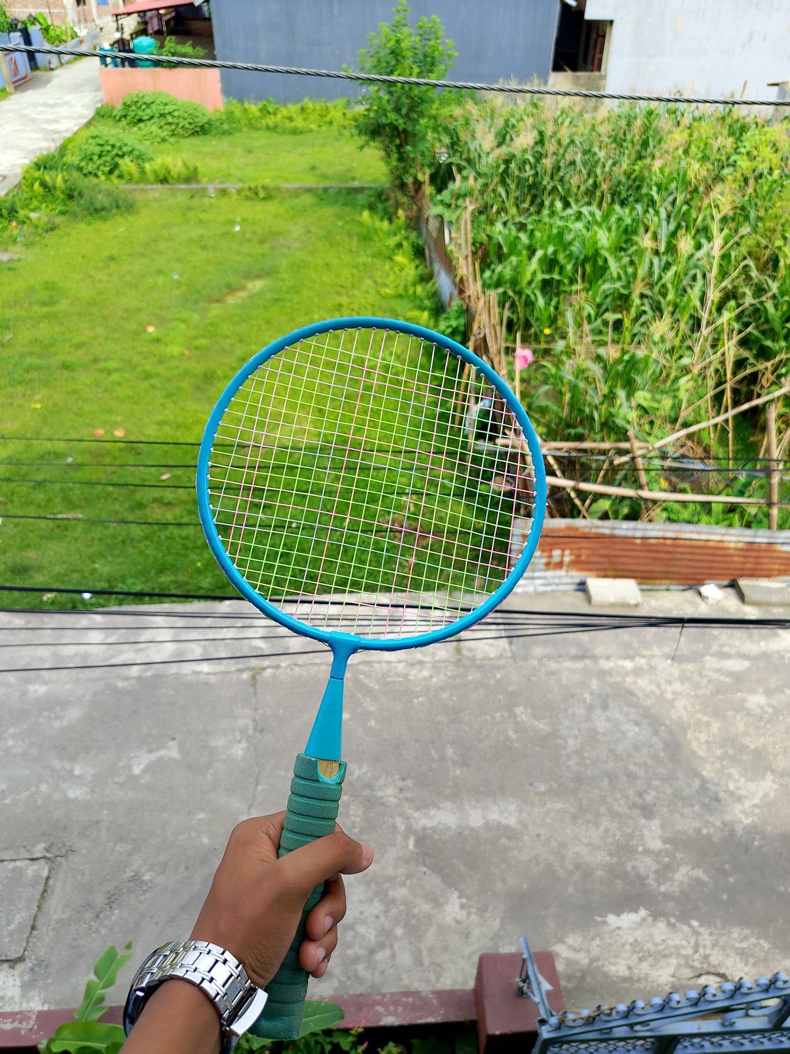 Elinde mavi badminton raketiyle yeşil bahçe manzarasına bakan spor tutkunu