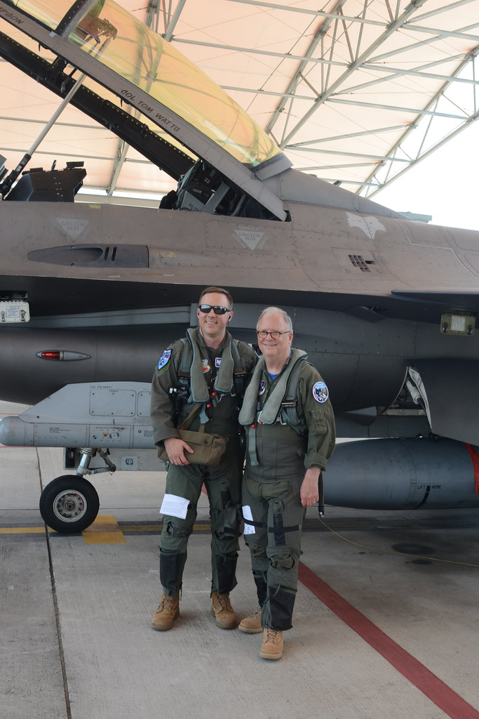 F-16 savaş uçağı önünde uçuş tulumlu iki askeri pilotun poz verdiği hangar fotoğrafı