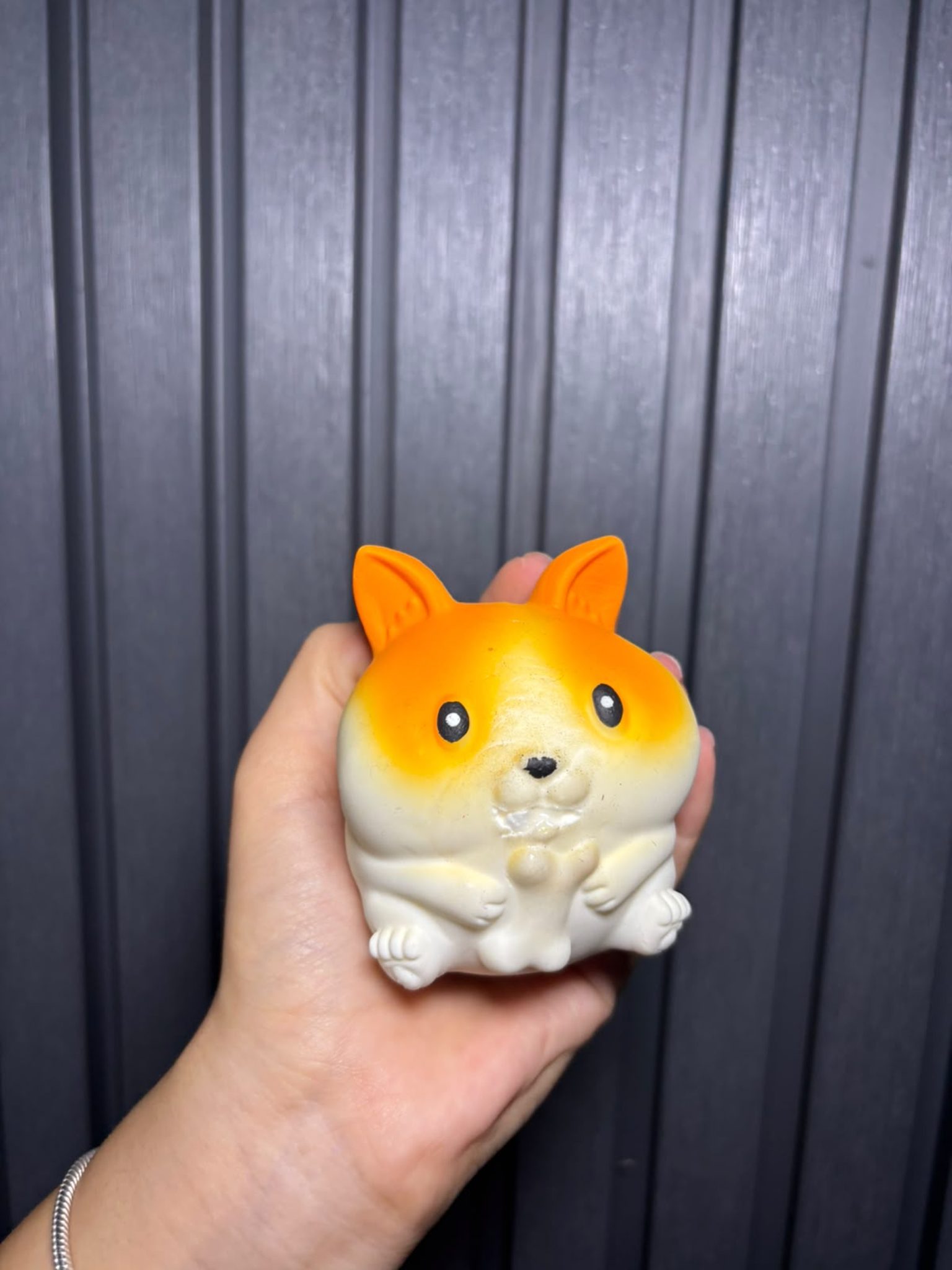 Gri arka plan önünde turuncu beyaz corgi desenli yumuşak oyuncak tutan el