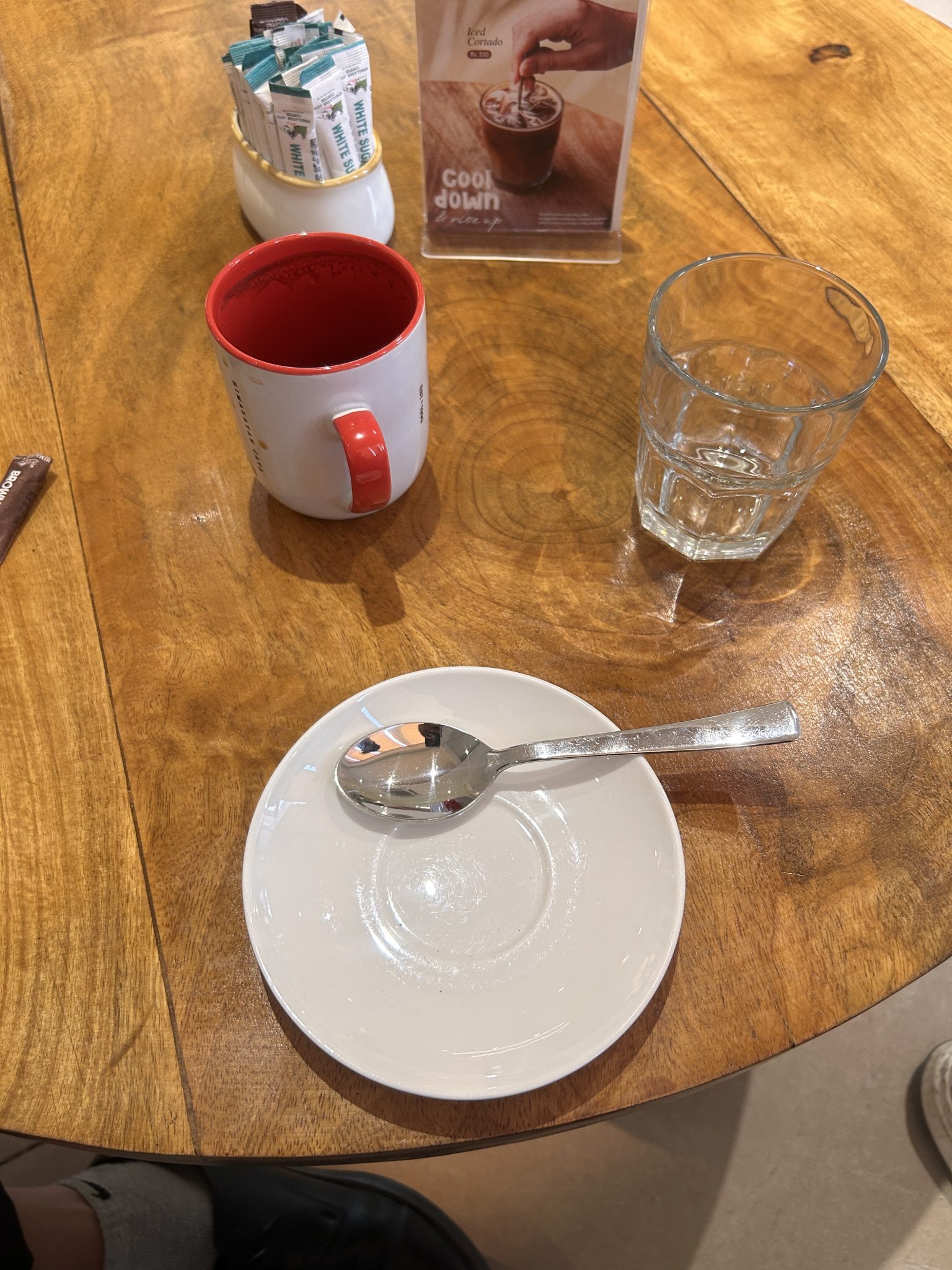 Kafe köşesinde ahşap masada kırmızı kupa, su bardağı ve boş tabak huzuru
