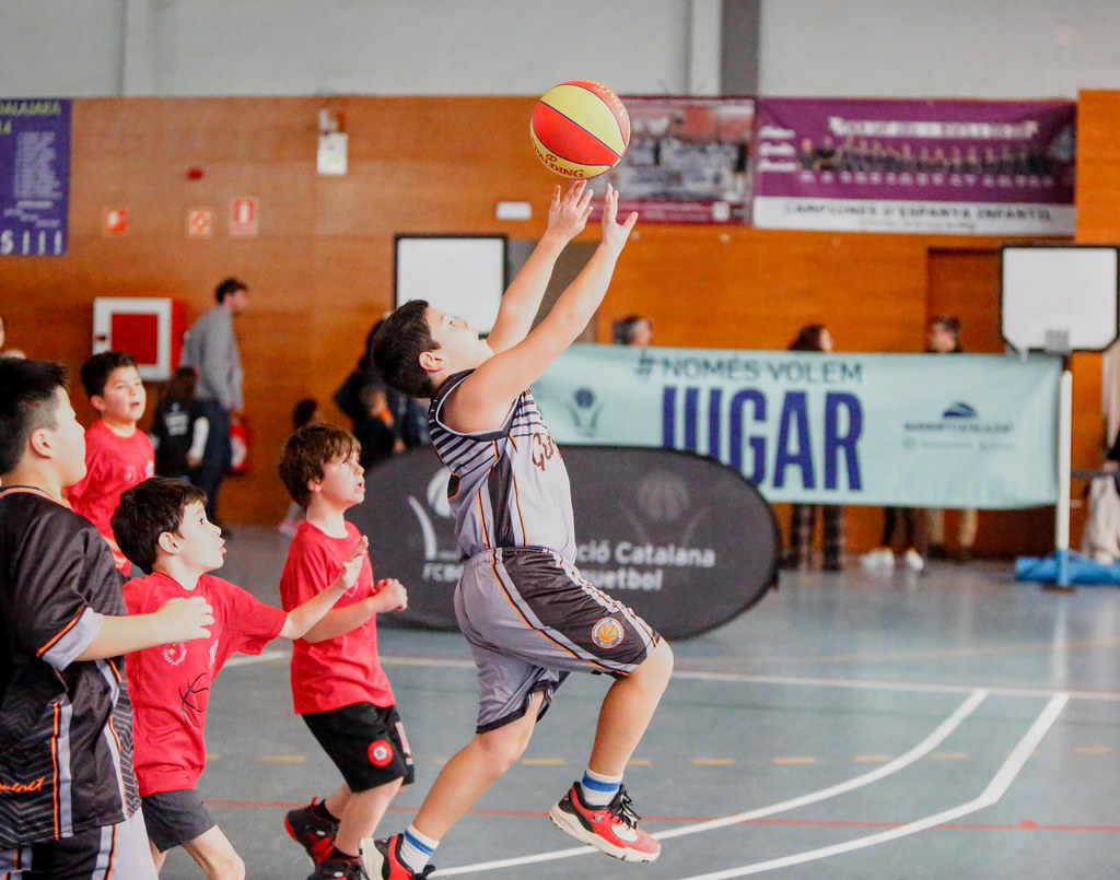Kapalı salonda basketbol maçı yapan çocukların enerjik anı ve atış hareketi