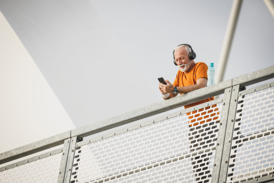 Kulaklıkla müzik dinleyen yaşlı adam köprüde telefonuna bakarken gülümsüyor