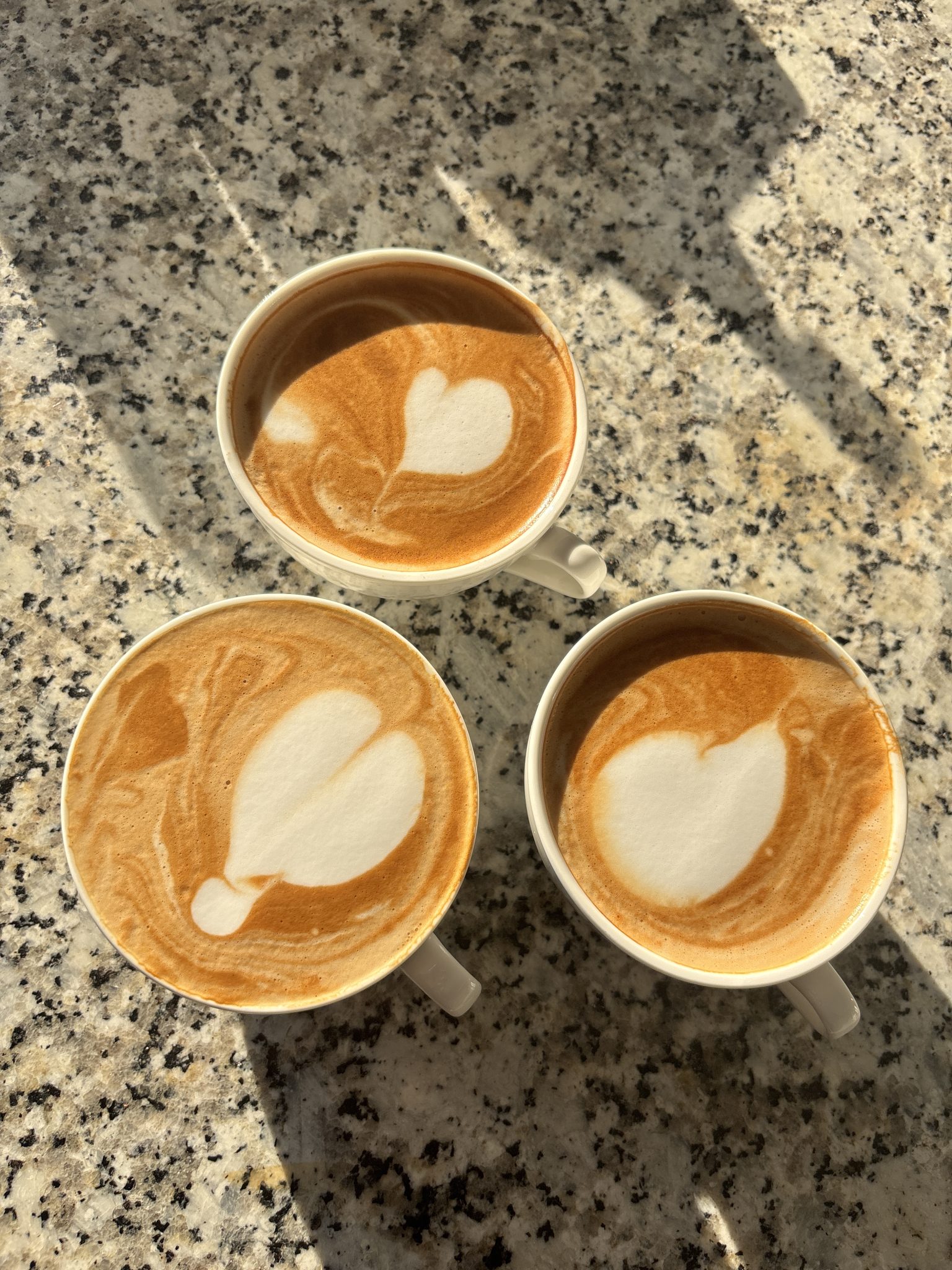 Mermer tezgahta üç fincan latte art ile gün ışığında kahve keyfi