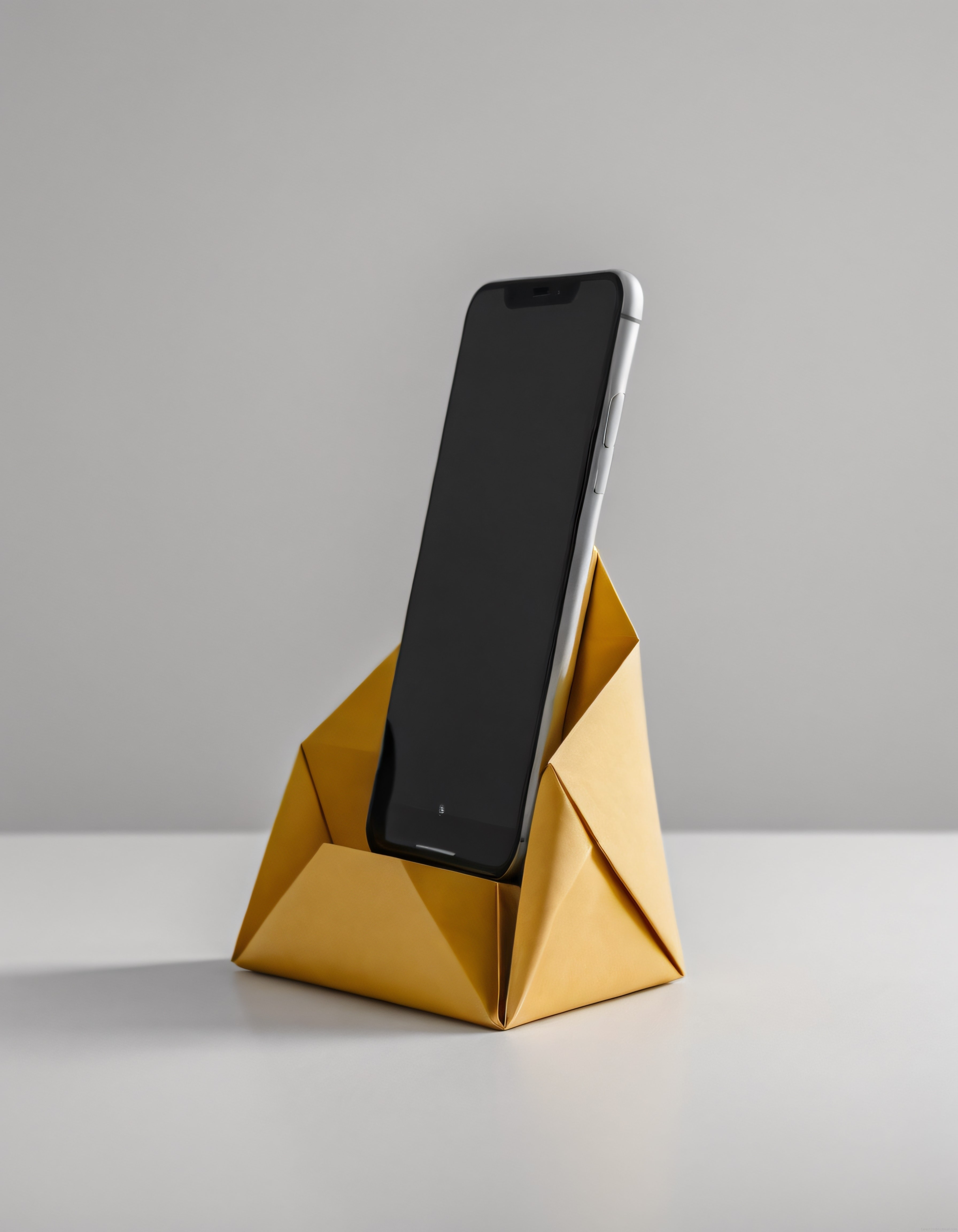 Minimalist ortamda sarı origami telefon standı ve siyah ekranlı akıllı telefon