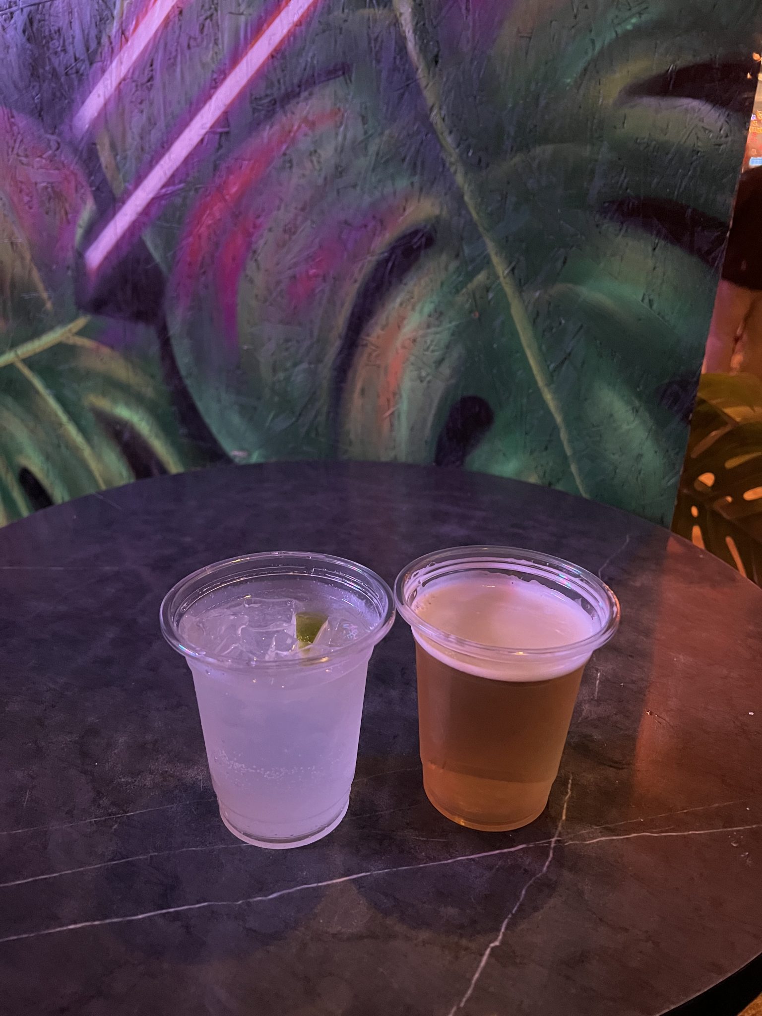 Neon ışıklı tropikal mekanda plastik bardakta bira ve limonlu kokteyl