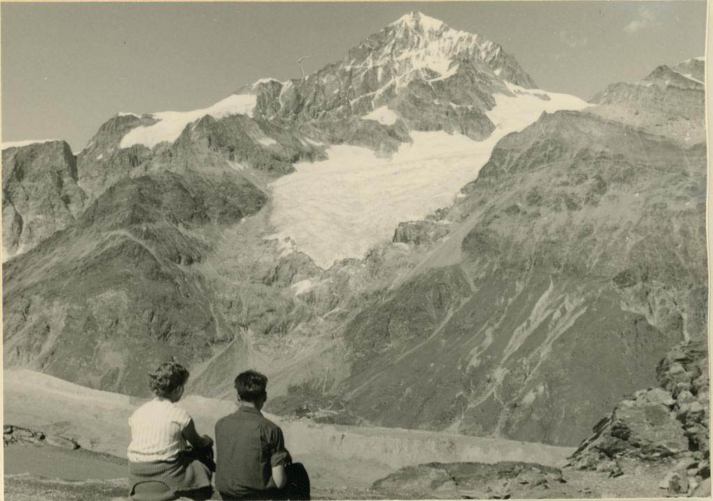 Nostaljik Kartpostal: Karlı Zirveli Dağlar ve Göl Kenarında Oturan İki İnsan