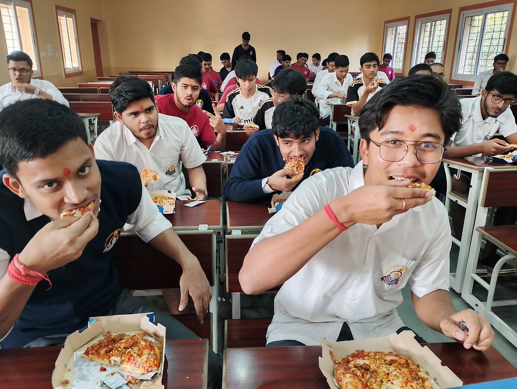 Okul sıralarında pizza yiyen genç öğrencilerin neşeli ve samimi anları