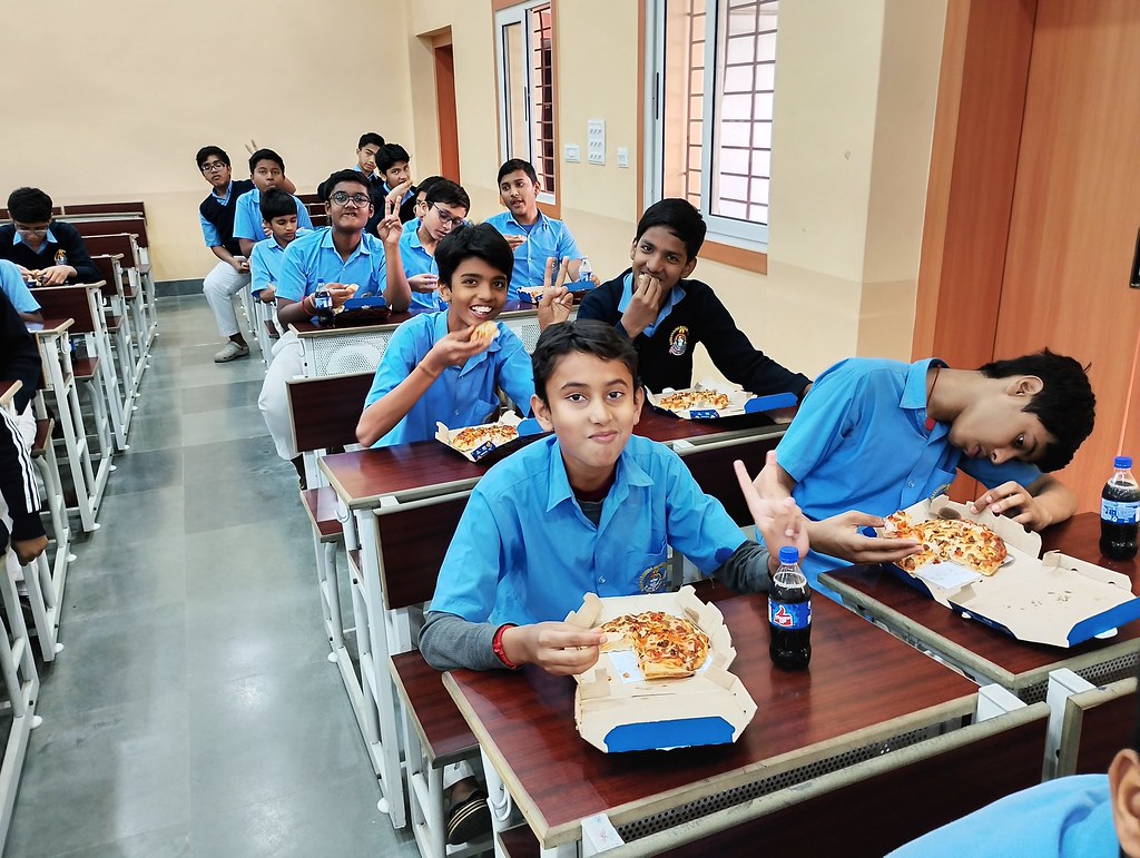 Okul sıralarında pizza yiyen öğrencilerin neşeli anları ve arkadaşlık hatırası
