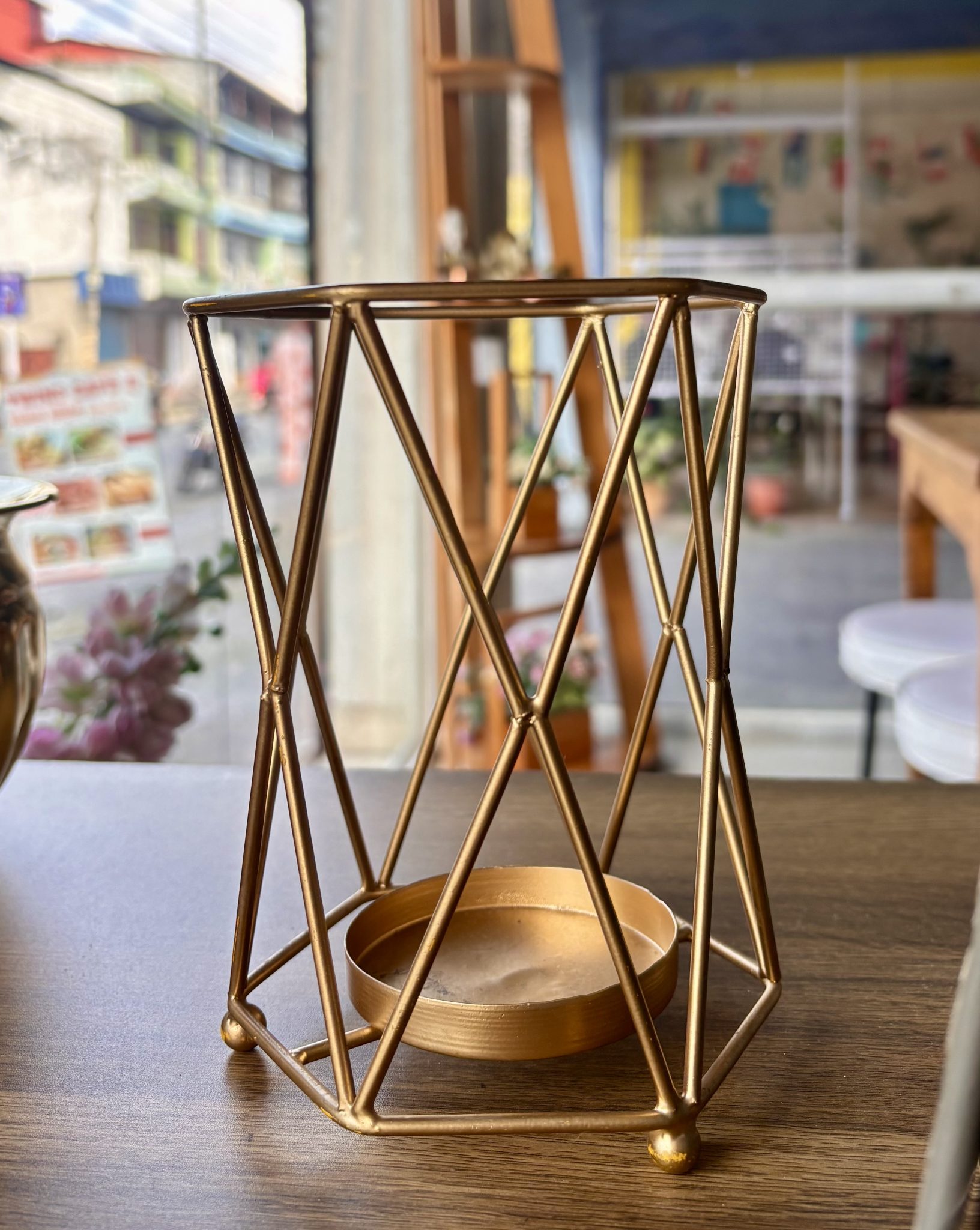 Şık pirinç rengi geometrik mumluk detayı ve sıcak kafe iç mekan arka planı