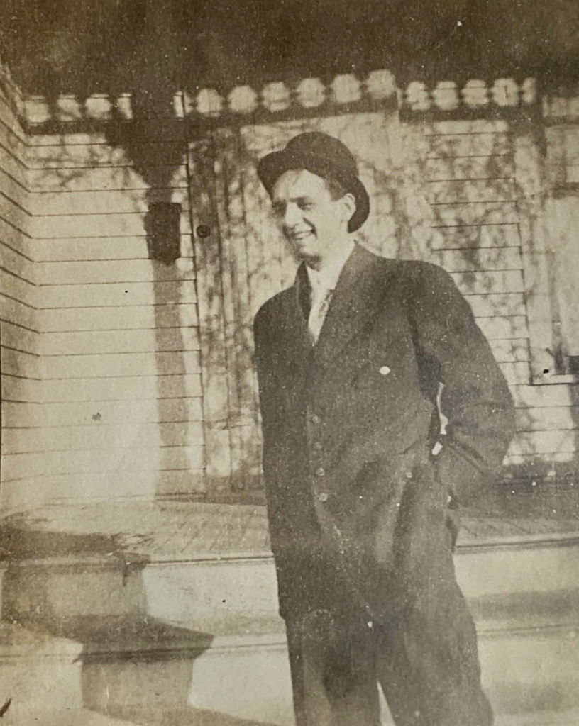 Takım elbiseli ve şapkalı adamın ahşap ev önündeki nostaljik portresi