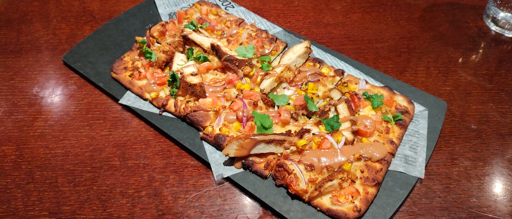 Taş fırında tavuklu ince hamur pizza, mısır ve taze yeşilliklerle rustik sunum