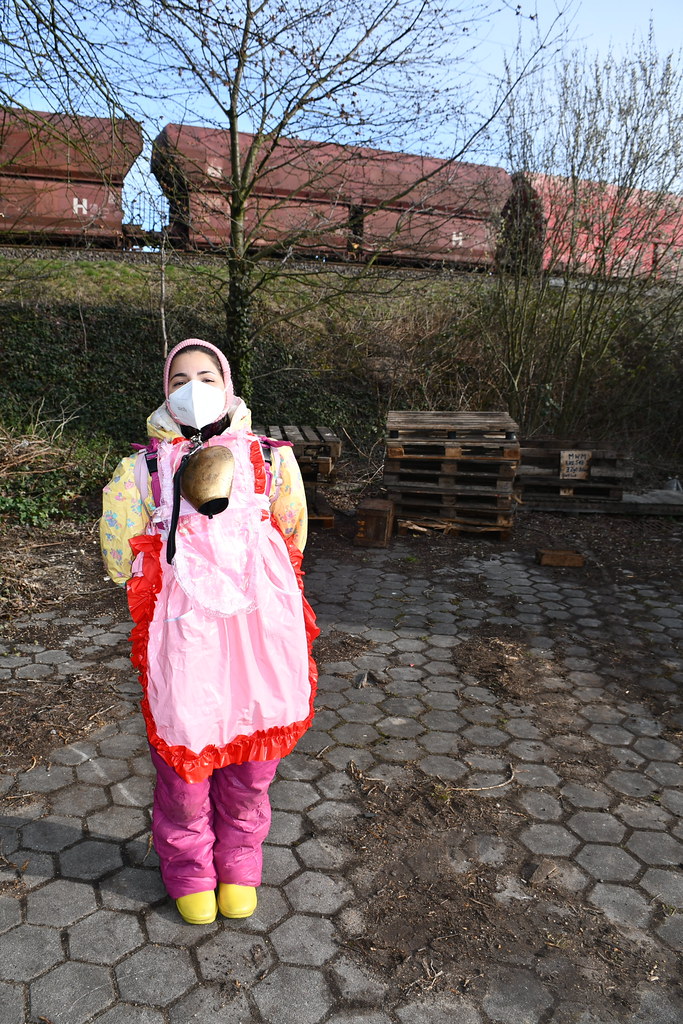 Tren yanında pembe önlük ve sarı ayakkabıyla duran maskeli kadın fotoğrafı