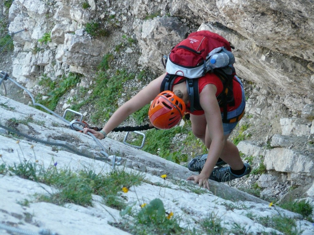 Turuncu kasklı kadın dağcı via ferrata rotasında zorlu kayalıkları tırmanıyor