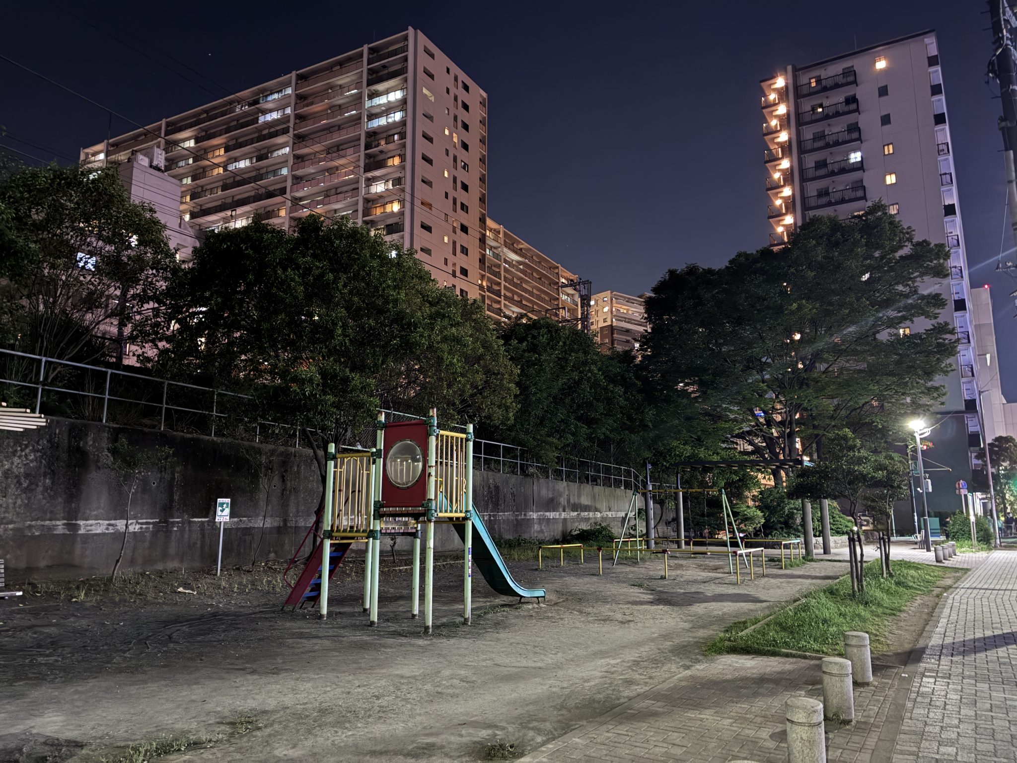 Yüksek Katlı Binaların Arasındaki Işıklı Gece Parkı ve Çocuk Oyun Alanı